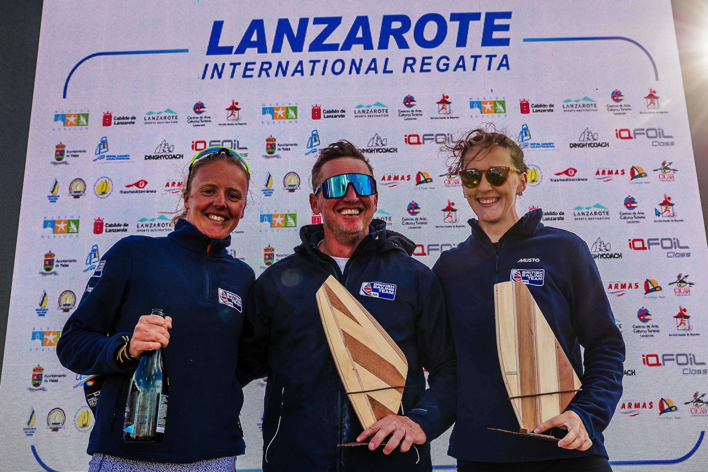 Emma Wilson (left) and Islay Watson celebrate their success with coach Sam Ross. ©Sailing Energy