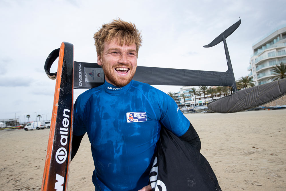 closeup of connor carrying his foiling kit on the shore, he is smiling