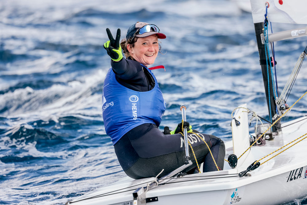 Hannah posing for picture while sailing in sailing dinghy, she is making a peace sign with her fingers